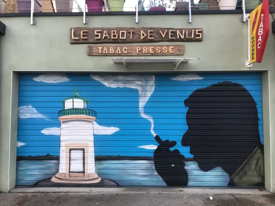 une peinture d'un fumeur devant le plus petit phare de france, sur une grille de tabac