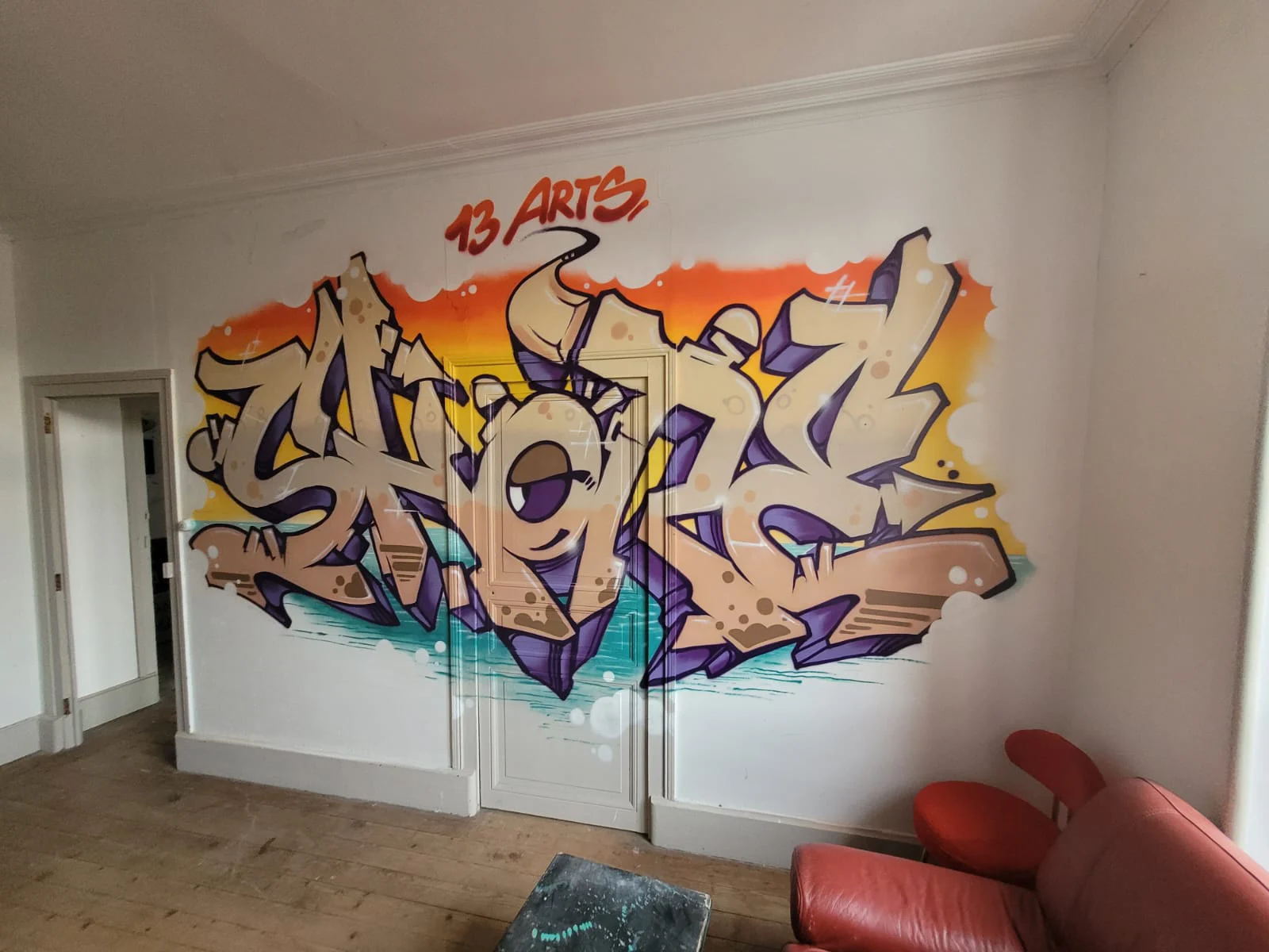 Fresque graffiti murale réalisée à l’intérieur des locaux de l’association 13 Arts, lettrage artistique style street art sur mur blanc avec dégradé orange et violet